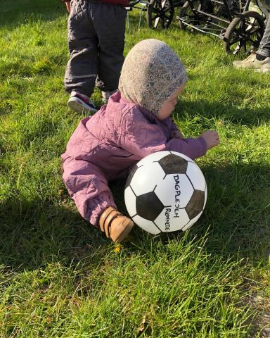 Et billede af et barn der sidder på græsset med en bold